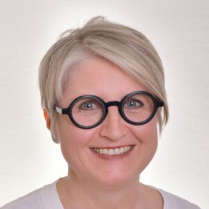 Portrait von Veronika Deuerling-Horváth. Blonder, asymmetrischer Kurzhaarschnitt, runde, schwarze Brille